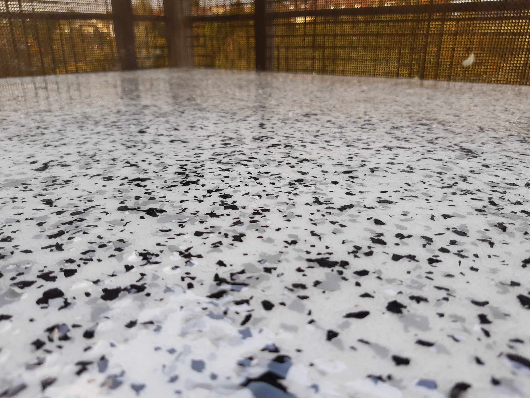 Biała posadzka żywiczna z czarnymi i szarymi płatkami, widoczna z niskiego kąta, z metalową balustradą w tle.
