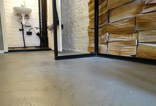 Szara, gładka posadzka w pomieszczeniu z białą cegłą i dekoracją imitującą drewno, widok z niskiej perspektywy.