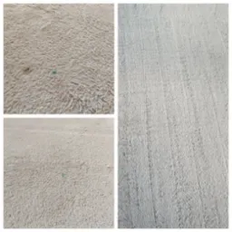 Fragment beżowego dywanu z długim włosiem, widoczne ślady po czyszczeniu, z bliska widoczny mały, niebieski punkt zabrudzenia.