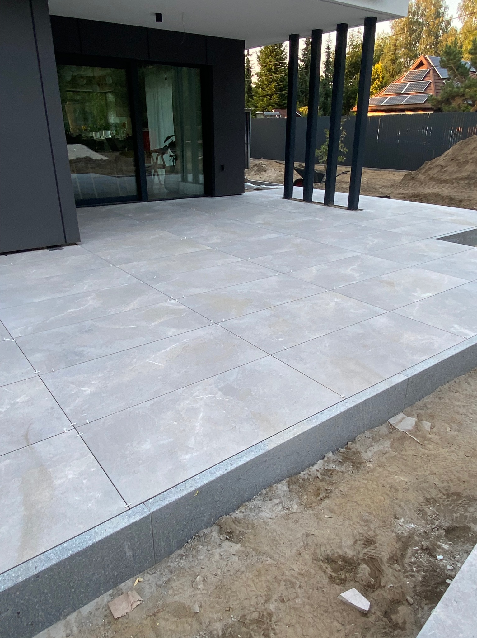 Jasnoszara, marmurkowa kostka ułożona na tarasie nowoczesnego domu z widocznymi dystansami między płytami i obrzeżem z szarego granitu.