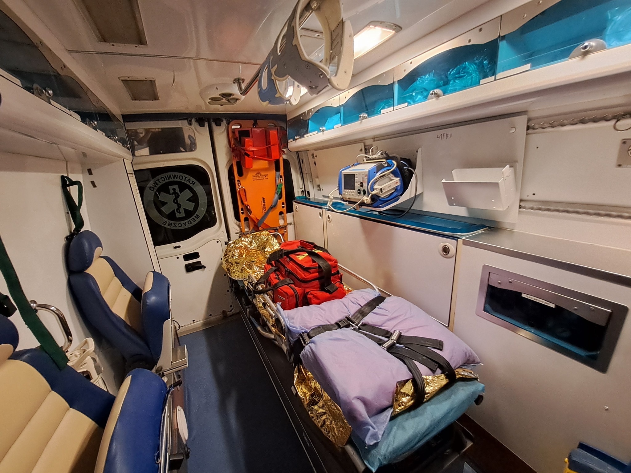 Wnętrze ambulansu z noszami, torbą medyczną, defibrylatorem i sprzętem ratunkowym.