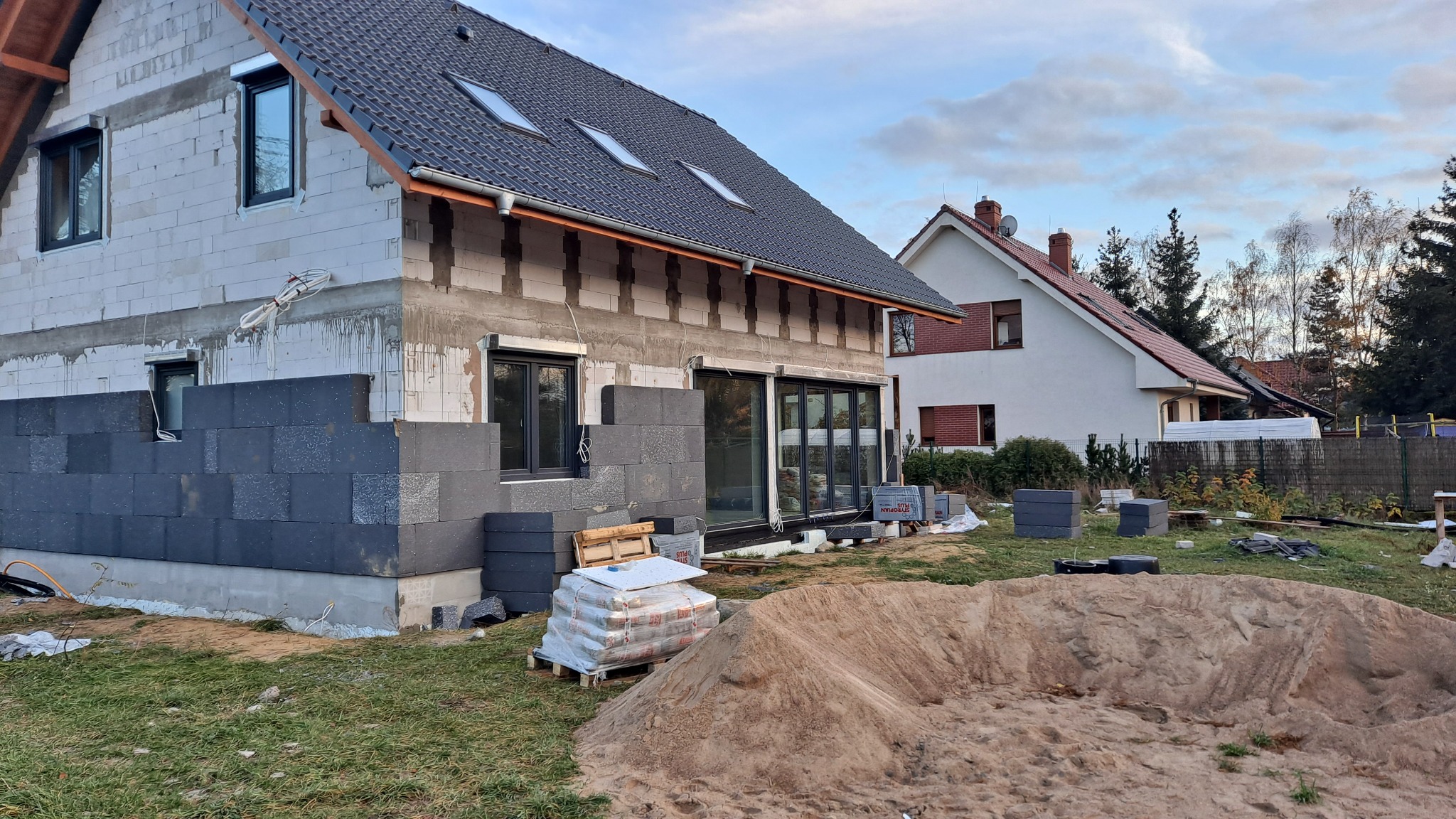 Budowa domu jednorodzinnego w Barlinku: wznoszenie ścian z bloczków betonowych, widoczne okna i przygotowany materiał budowlany.