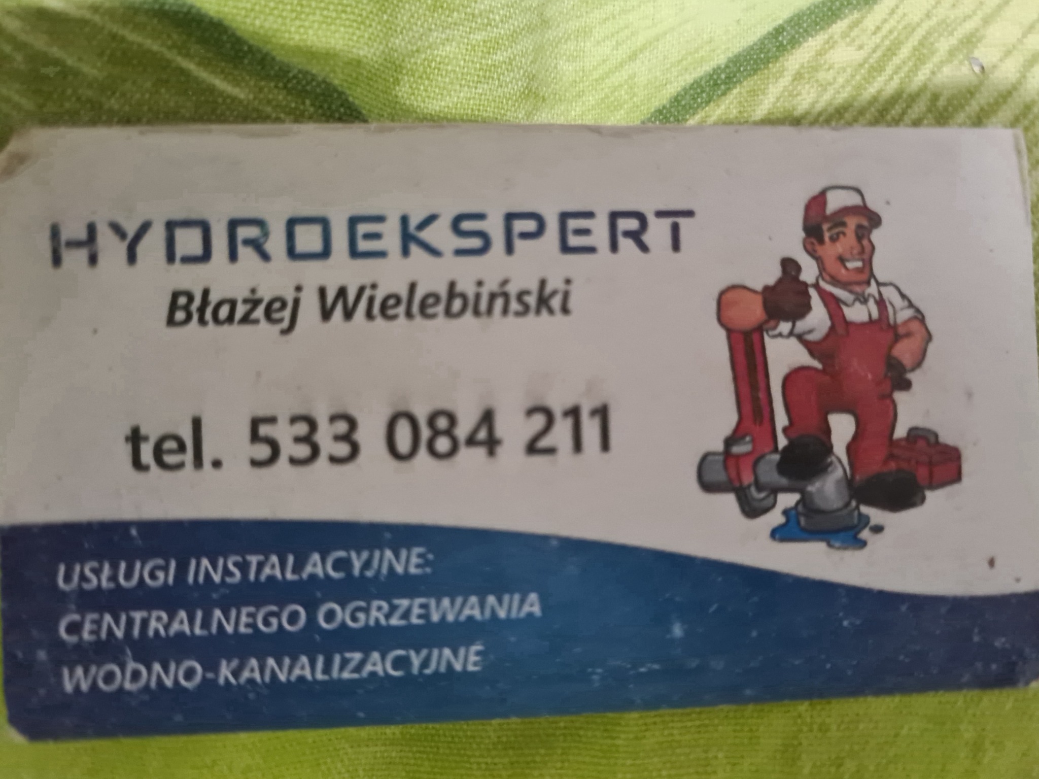 Wizytówka firmy Hydroekspert Błażej Wielebiński z numerem telefonu i ilustracją hydraulika z kluczem do rur.