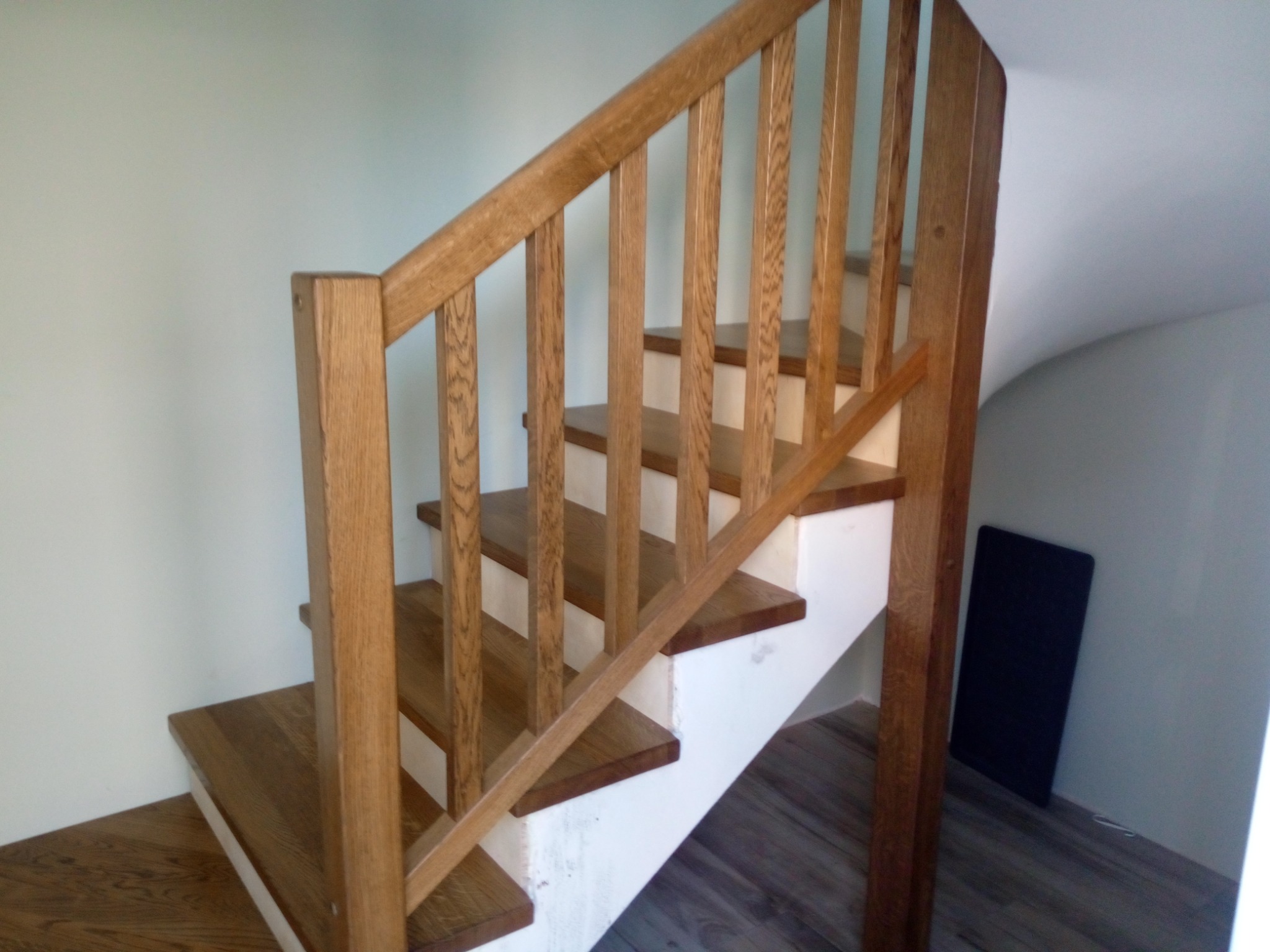 Klasyczne schody z drewna dębowego z białymi podstopnicami, z prostą balustradą w jasnym wnętrzu.