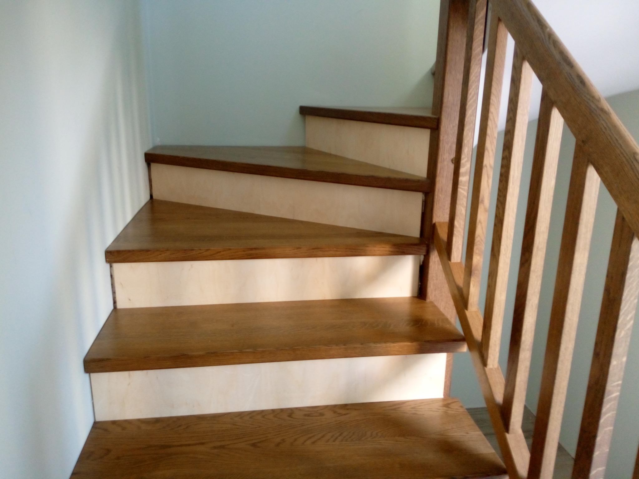 Jasne, drewniane schody z dębowymi stopniami i jasnymi podstopnicami, z drewnianą balustradą, widok z dołu.