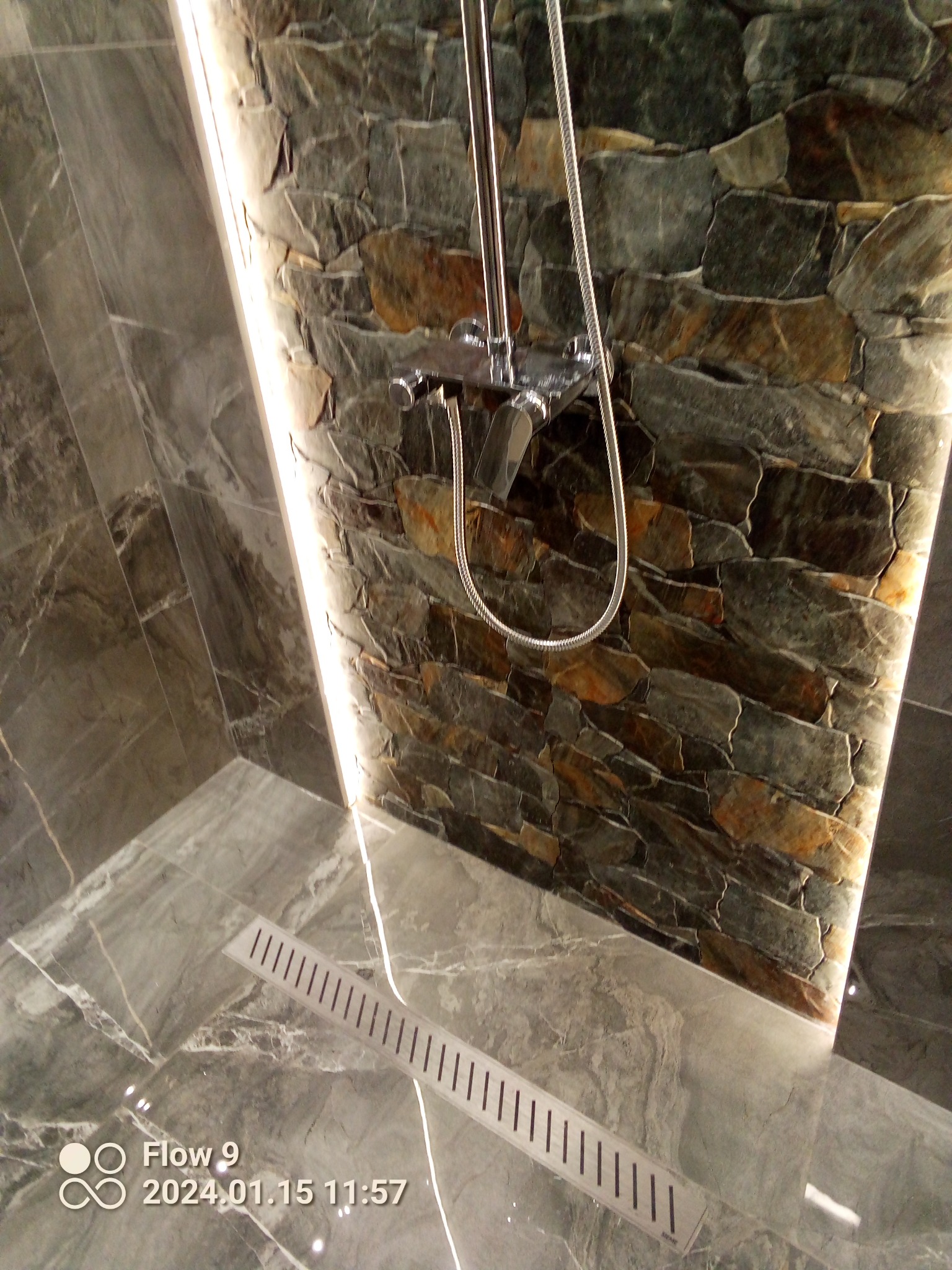 Nowoczesna kabina prysznicowa z kamienną ścianą podświetloną LED, marmurowe płytki podłogowe z odpływem liniowym.