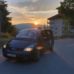 Czarny van taxi Renault Espace na tle zachodzącego słońca i górskiego krajobrazu, z widocznym znakiem taxi na dachu i numerem rejestracyjnym SCI 5421J.