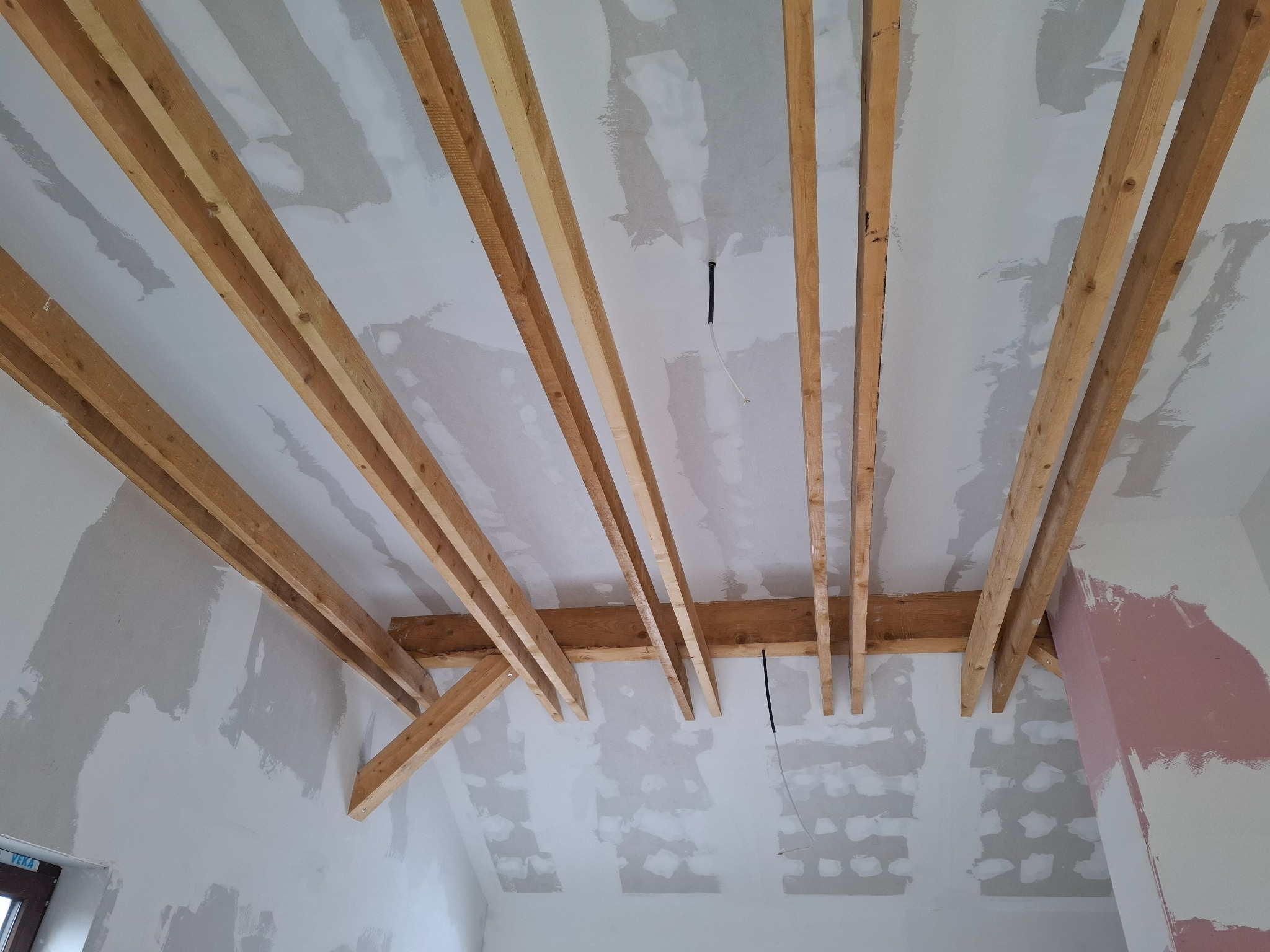 Konstrukcja drewniana pod sufitem podwieszanym z płyt kartonowo-gipsowych, widoczne przewody elektryczne, ściany w trakcie szpachlowania.