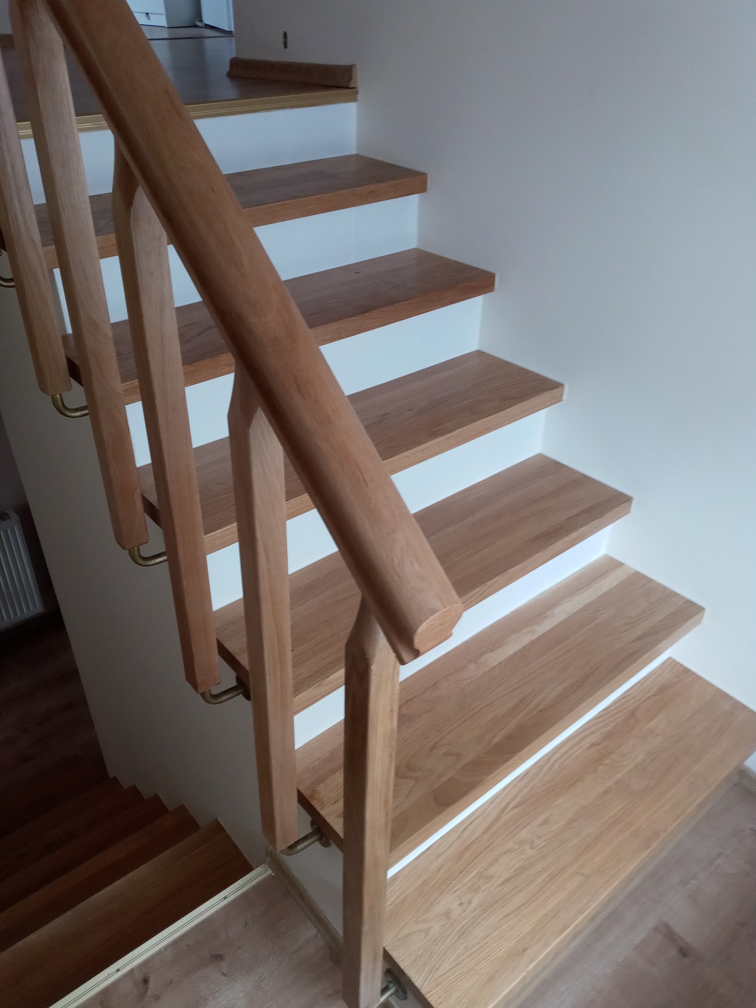 Jasne drewniane schody z białymi podstopnicami i drewnianą balustradą z metalowymi uchwytami, widok z góry.