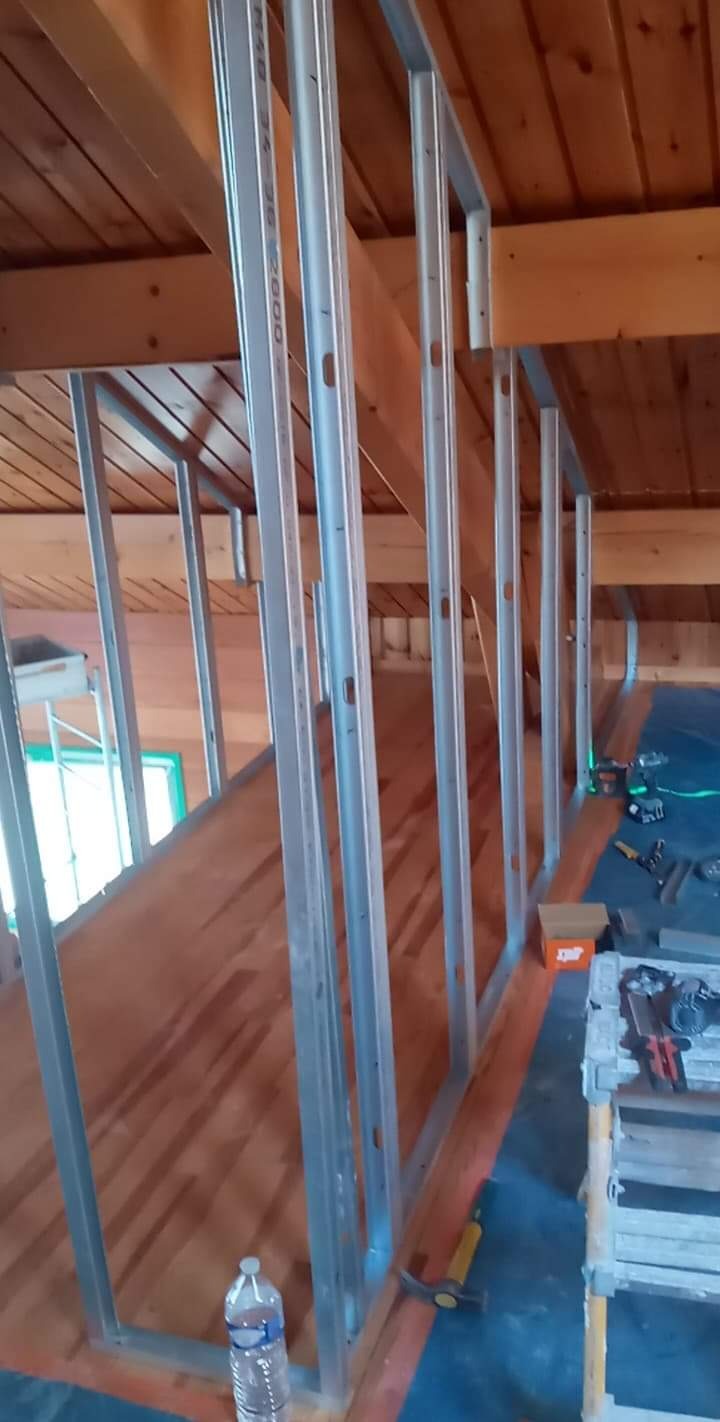 Konstrukcja szkieletowa z profili stalowych, przygotowana do montażu płyt gipsowo-kartonowych na poddaszu z drewnianym stropem; widoczne narzędzia i butelka wody.
