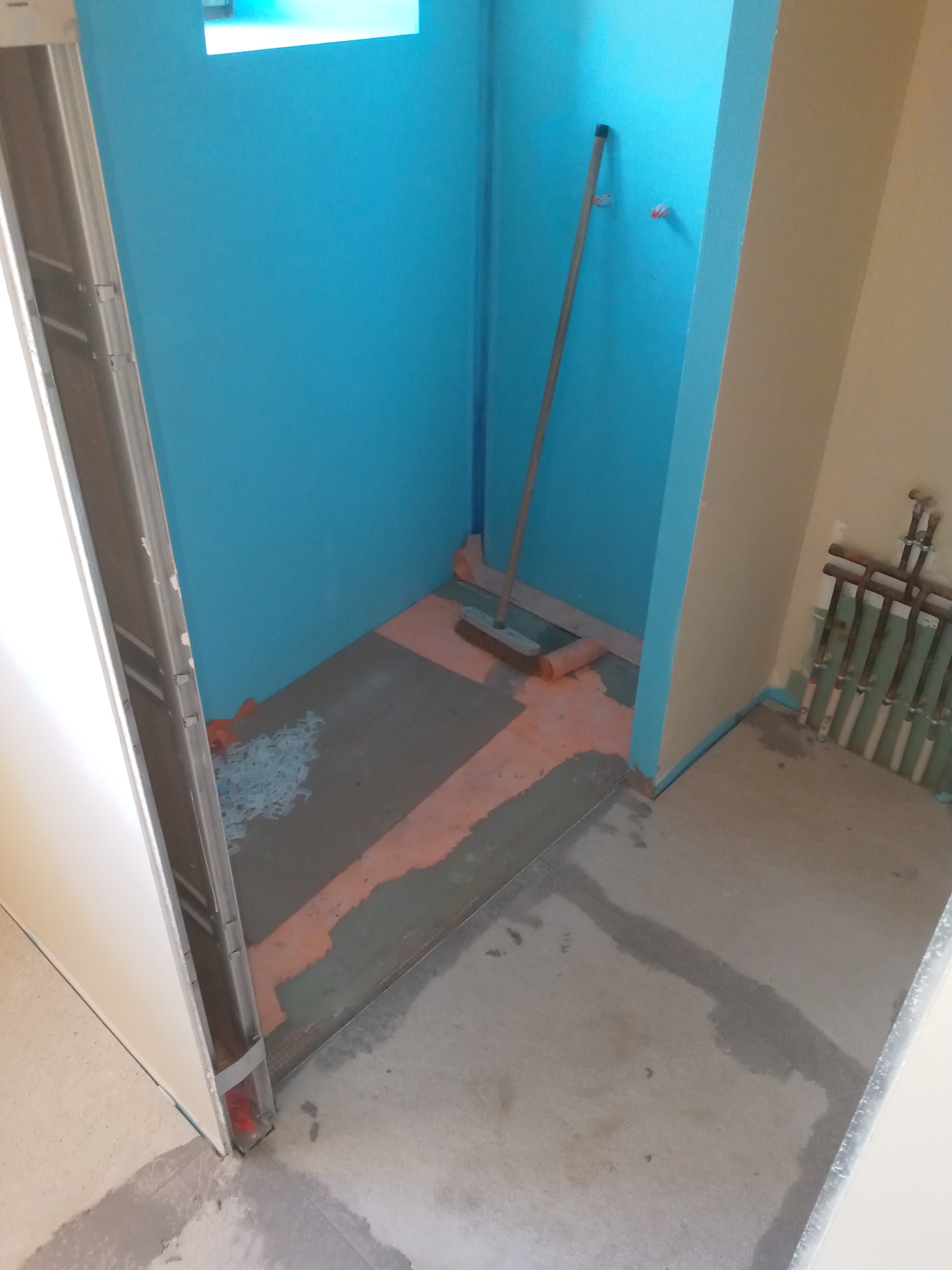 Przygotowanie do układania płytek w kabinie prysznicowej w Nidzicy. Widoczne hydroizolacja na ścianach, wylewka na podłodze, krzyżyki dystansowe i narzędzia.