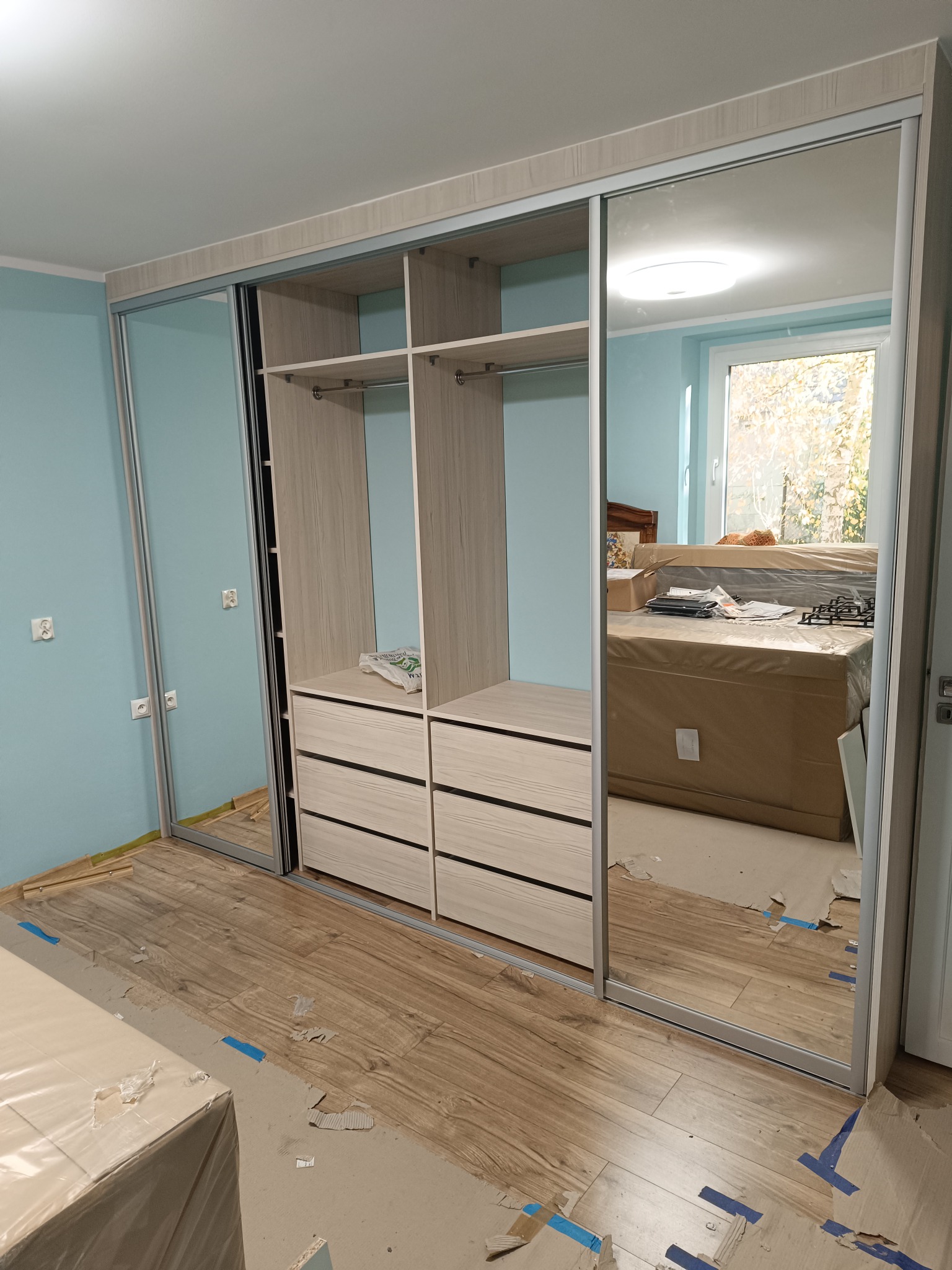Montaż szafy wnękowej z lustrzanymi drzwiami przesuwnymi w Bierutowie, widoczne zabezpieczenia podłogi podczas prac.