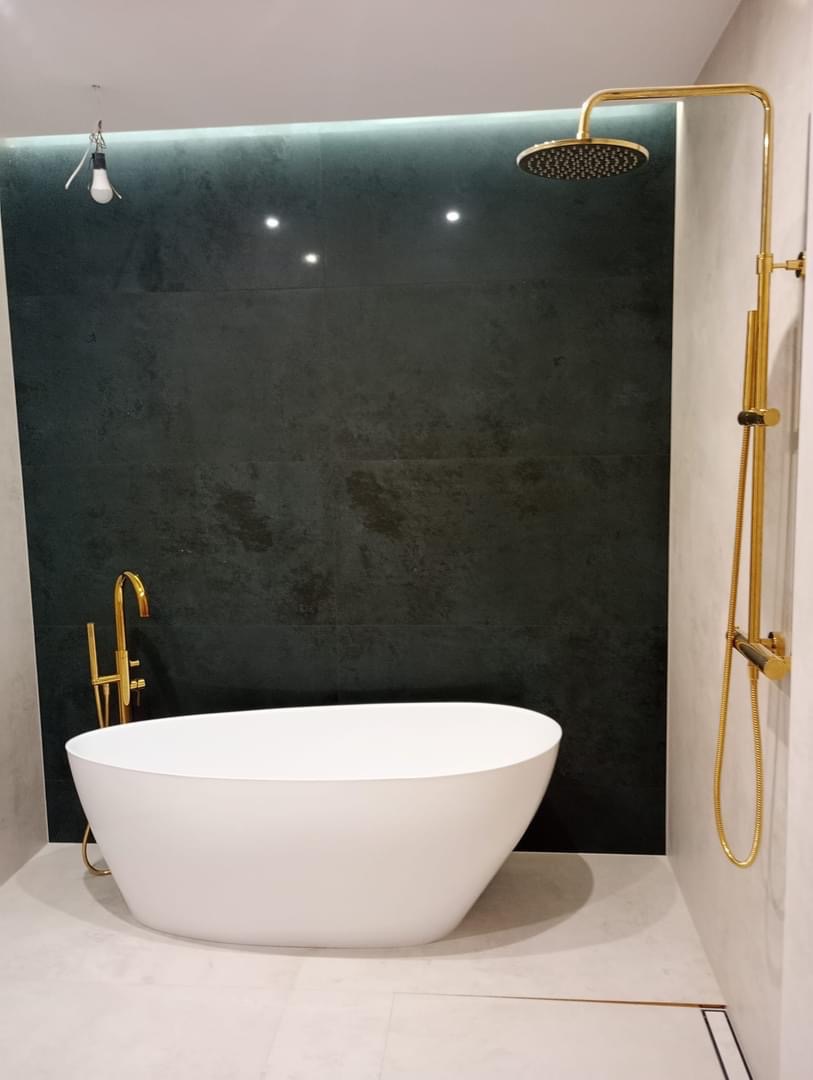 Nowoczesna łazienka: wolnostojąca biała wanna, złota armatura, ciemnozielone płytki z podświetleniem LED, minimalistyczny odpływ liniowy w podłodze.