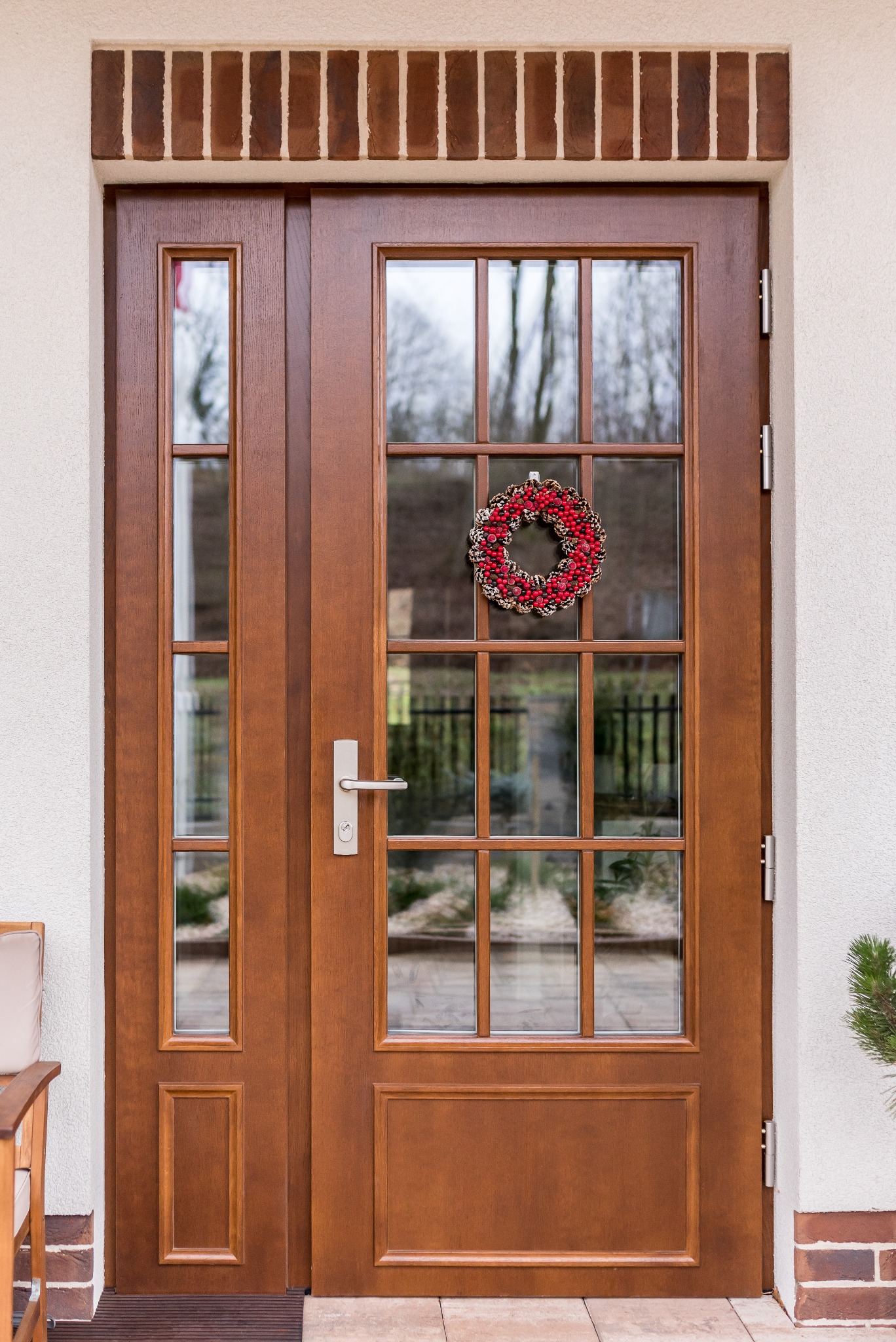 Dwuskrzydłowe, brązowe drzwi wejściowe z szybami i dekoracyjnym wieńcem zawieszonym na jednej z nich, widoczne z zewnątrz domu.