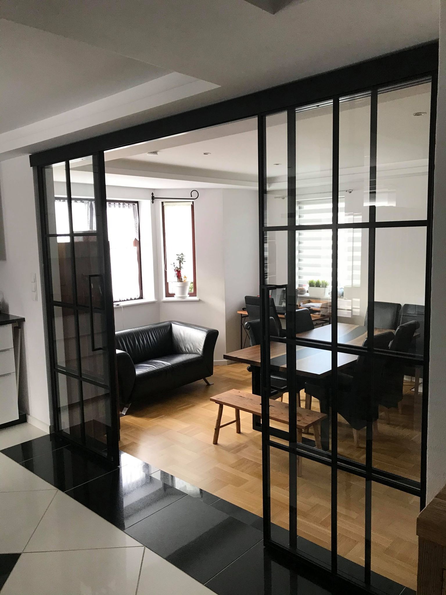 Przeszklone drzwi przesuwne w stylu loftowym oddzielające salon od jadalni w mieszkaniu w Szczecinie, z widoczną czarną ramą i podziałami szprosami.