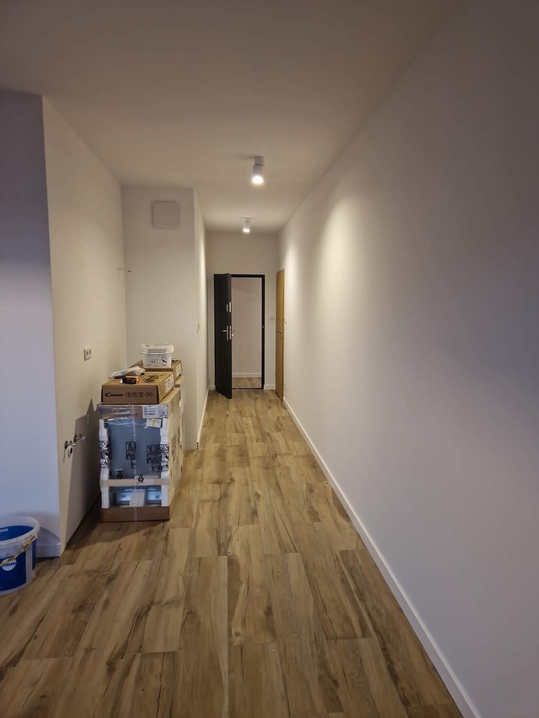 Korytarz po remoncie z ułożonymi panelami podłogowymi w odcieniach drewna, świeżo pomalowanymi białymi ścianami i przygotowanymi materiałami budowlanymi w kartonach.