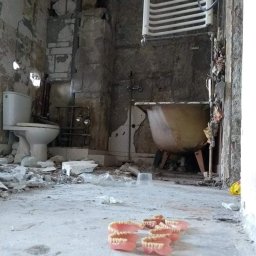 MATBUD - Łazienka w trakcie demontażu: widoczne gruz, odłączona toaleta, stara wanna na nóżkach i grzejnik drabinkowy, a na pierwszym planie protezy dentystyczne.