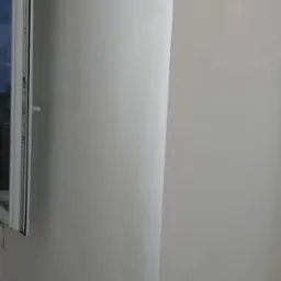 Świeżo pomalowana ściana w odcieniach bieli z widocznym fragmentem okna PCV po lewej stronie, ukazująca gładką powierzchnię po remoncie.