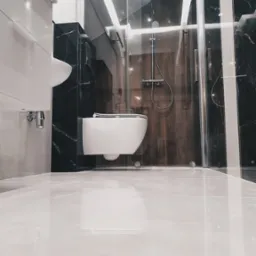 Nowoczesna łazienka z kabiną prysznicową ze szklanymi drzwiami, wiszącą miską WC i umywalką, wykończona płytkami imitującymi czarny marmur z białymi żyłami i błyszczącymi białymi płytkami podłogowymi.