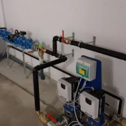 Złożona instalacja hydrauliczna z niebieskim zbiornikiem ciśnieniowym, czarnymi rurami i białymi urządzeniami sterującymi, zamontowana w pomieszczeniu technicznym.