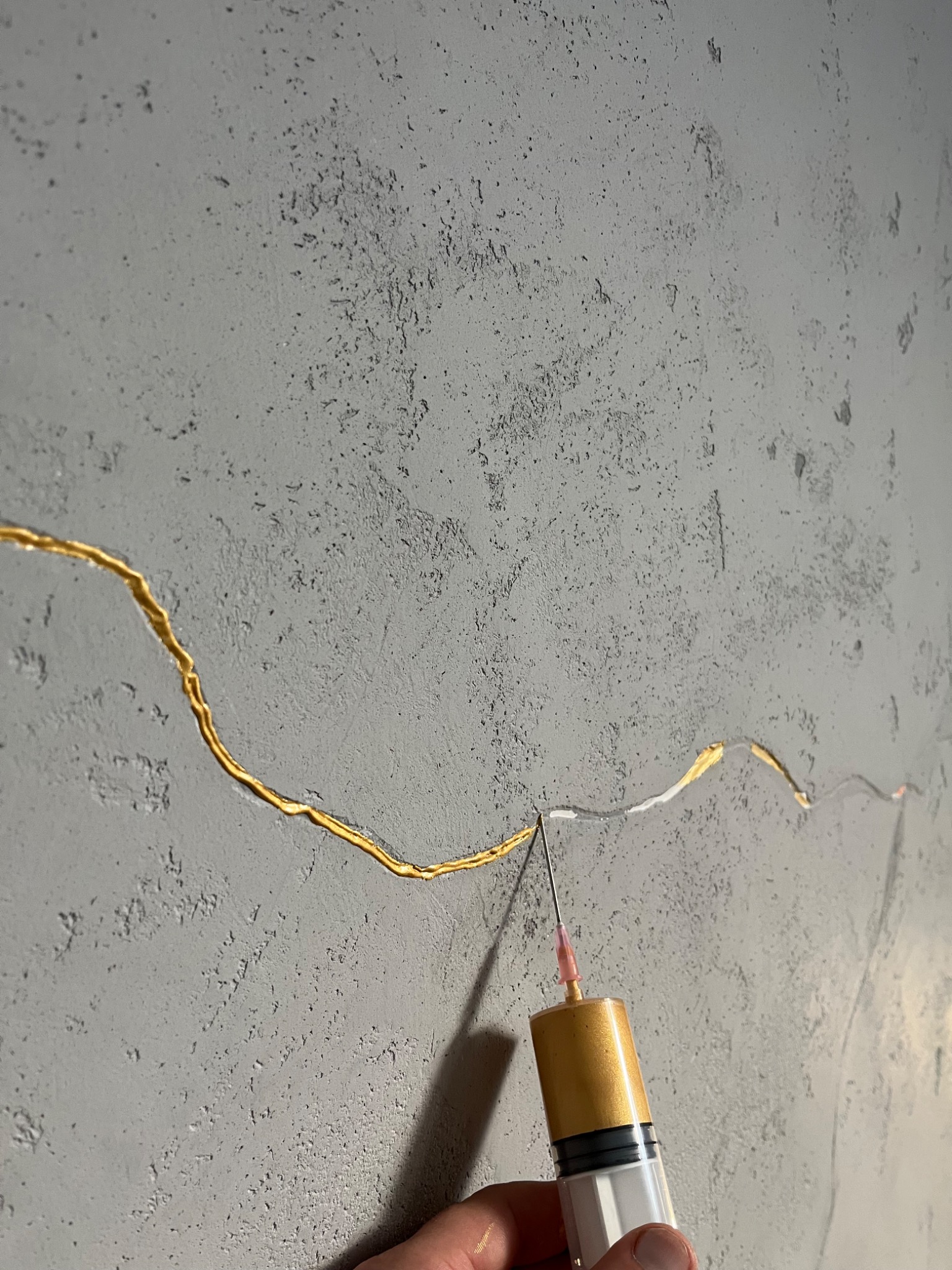 Aplikacja złotej żywicy na szpachlowaną ścianę w Brzezówce za pomocą strzykawki z igłą, imitująca japońską technikę Kintsugi, z bliska.