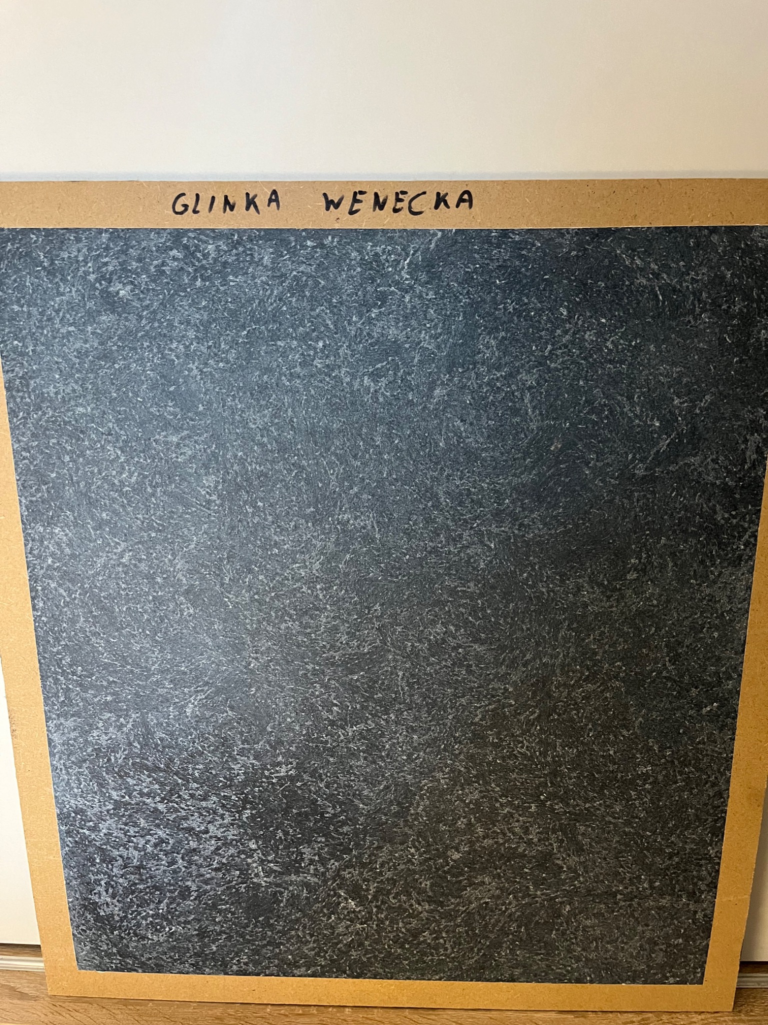 Próbka 'Glinka Wenecka' na płycie MDF, prezentująca szaro-czarną strukturę z delikatnym połyskiem, imitującą naturalny kamień.