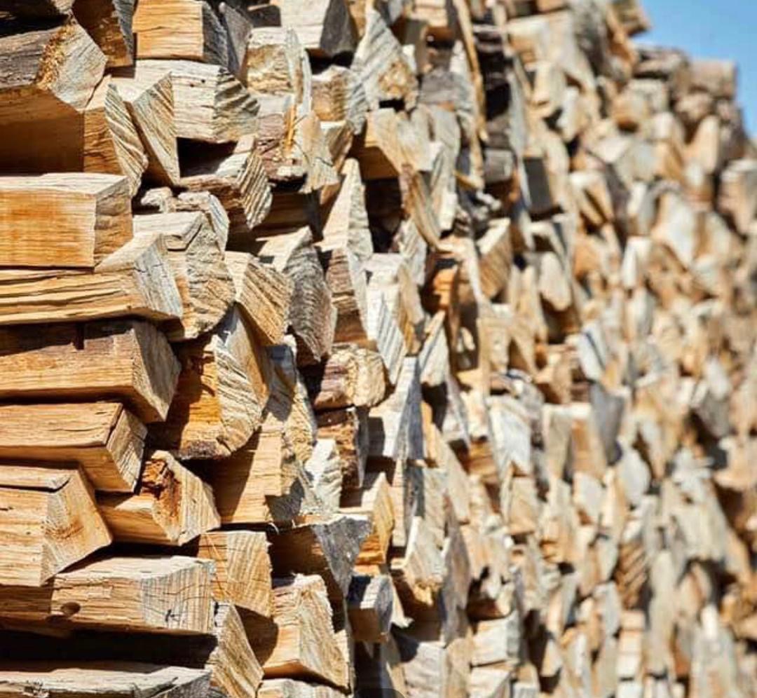 Rząd równo ułożonych, pociętych kawałków drewna na opał, z widocznymi słojami i różnymi odcieniami brązu, tworzących uporządkowany stos.
