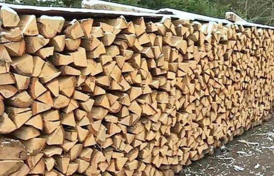 Równomiernie ułożony stos pociętego drewna na opał, z widocznymi śladami śniegu na górze i u podstawy.