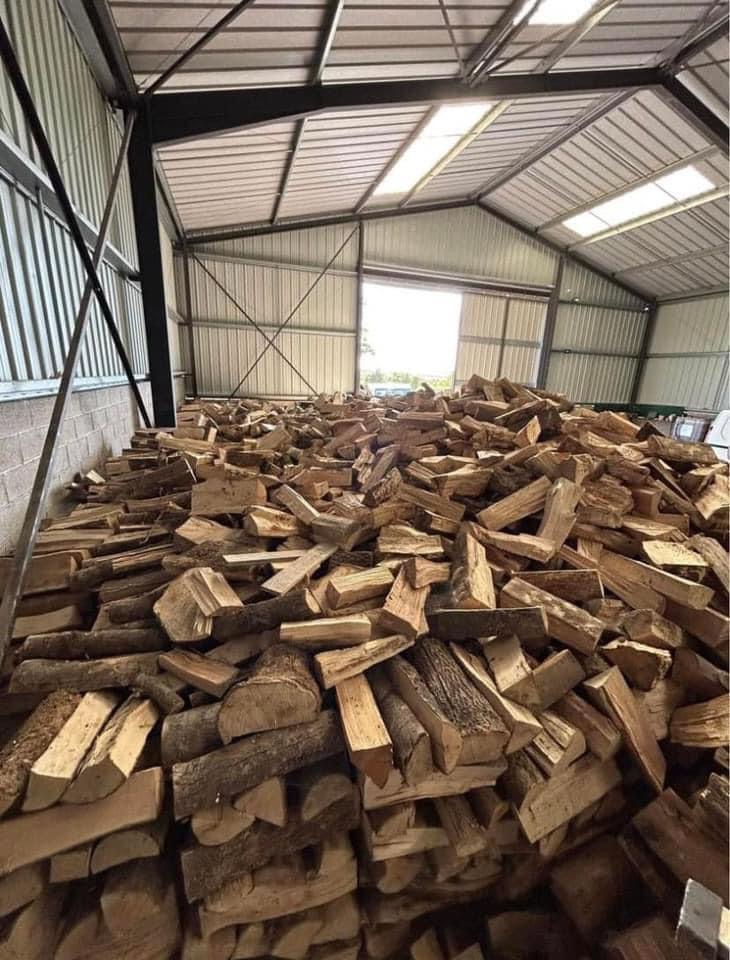 Stos pociętego drewna w metalowym magazynie z otwartymi wrotami, widok z dołu.