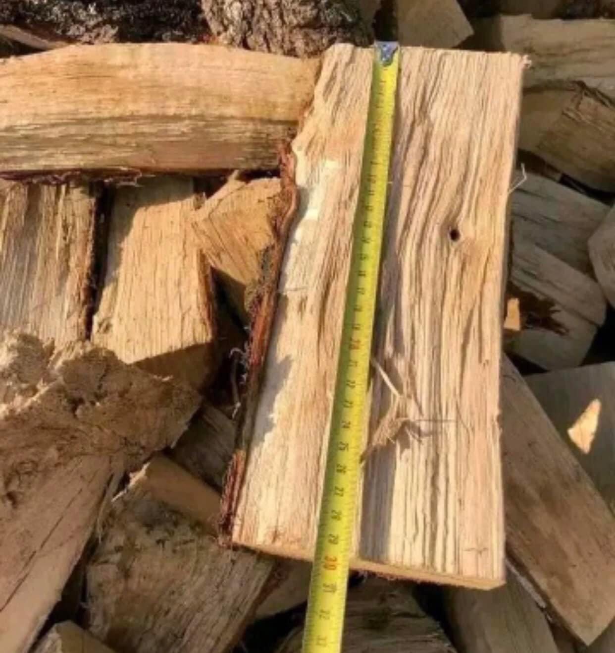 Stos pociętego drewna ułożonego na ziemi, z żółtą miarką przyłożoną do jednego kawałka, ukazującą jego wymiary.
