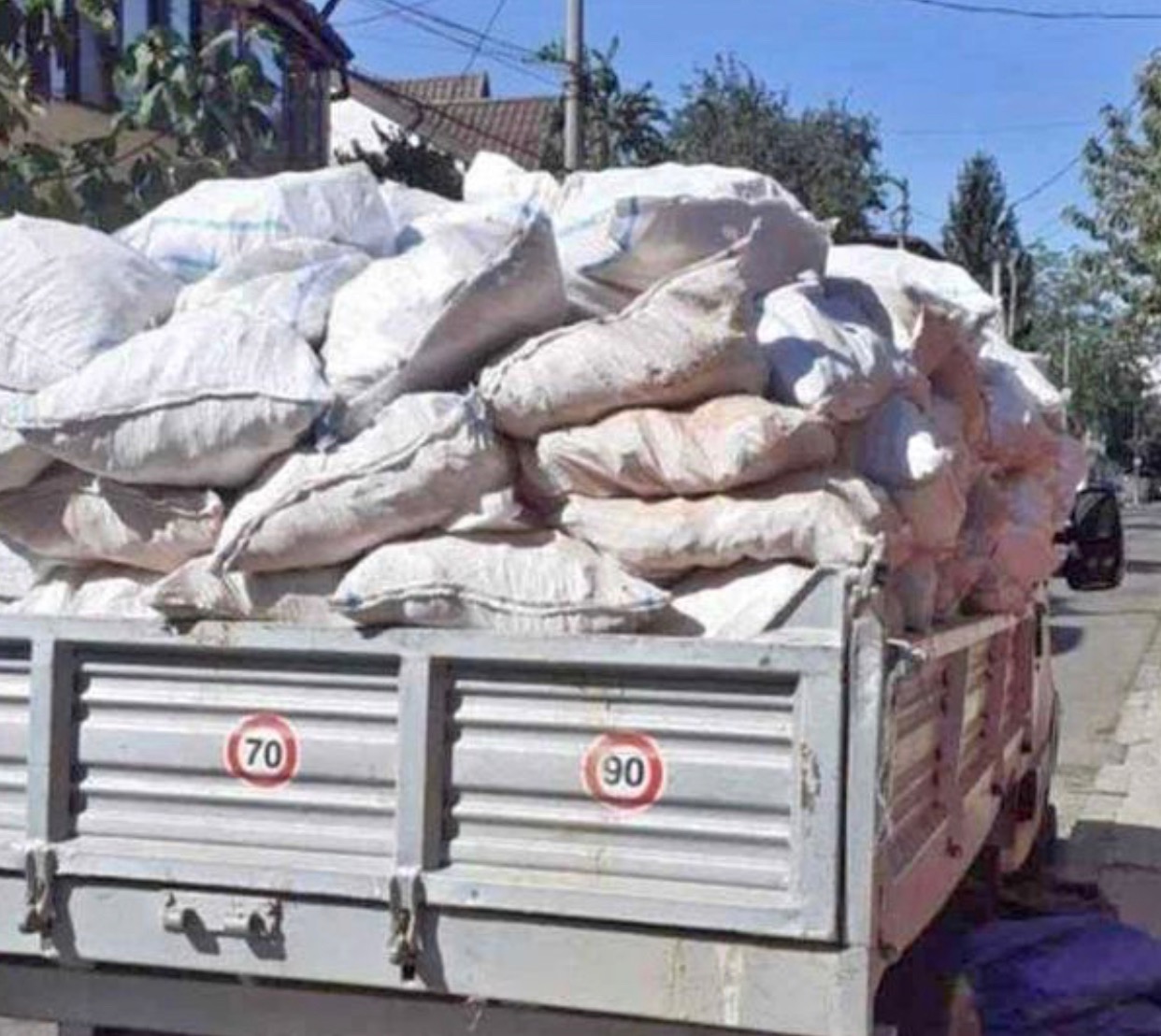 Ciężarówka z przeładowaną skrzynią wypełnioną workami z nieznaną zawartością, widoczne znaki ograniczenia prędkości 70 i 90 km/h na boku skrzyni.