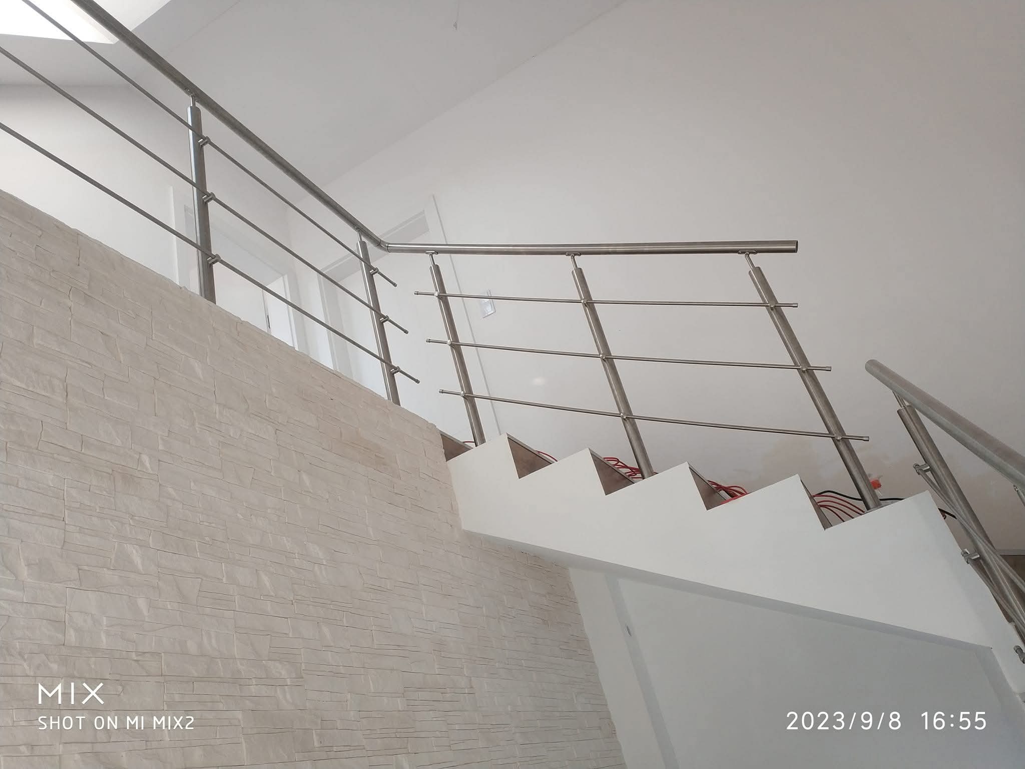 Wnętrze z nowymi schodami z poręczami ze stali nierdzewnej, widok z dołu, pokazujący detale montażu i wykończenia. Ściana wyłożona dekoracyjną okładziną imitującą kamień.