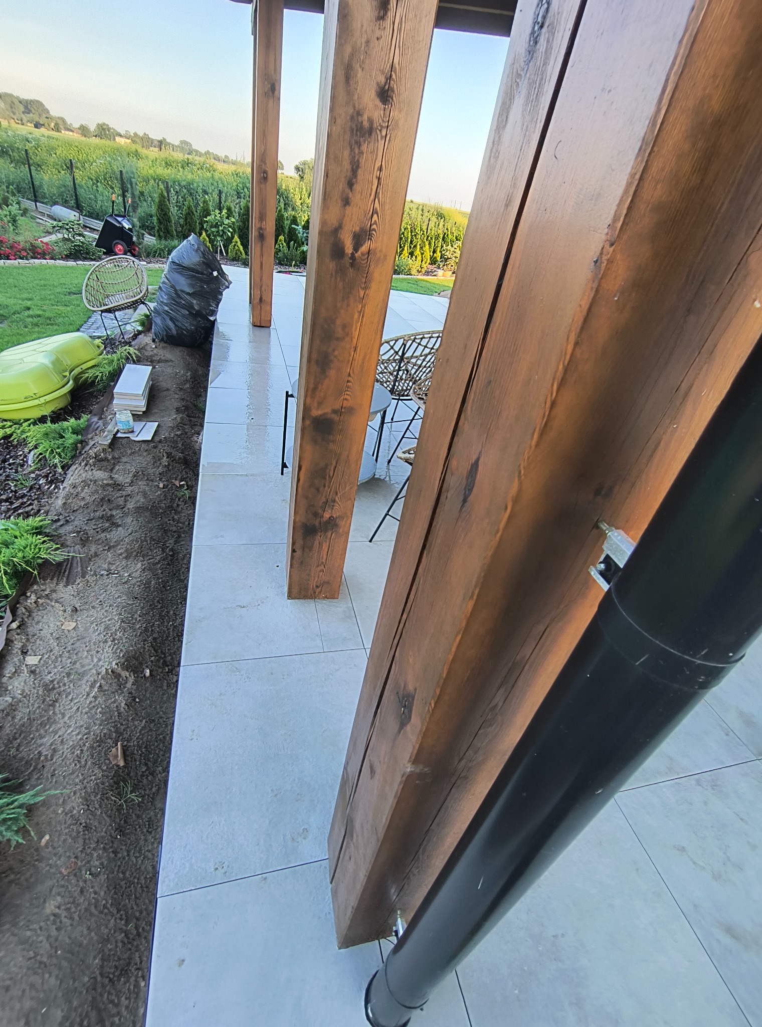 Konstrukcja pergoli z ciemnego drewna, z widocznym systemem odprowadzania wody, na tle zieleni ogrodu i nieba. Widok z dołu, podkreślający solidność wykonania.