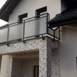 Nowoczesna balustrada ze szkła i czarnego metalu na balkonie domu z elewacją z cegieł dekoracyjnych.