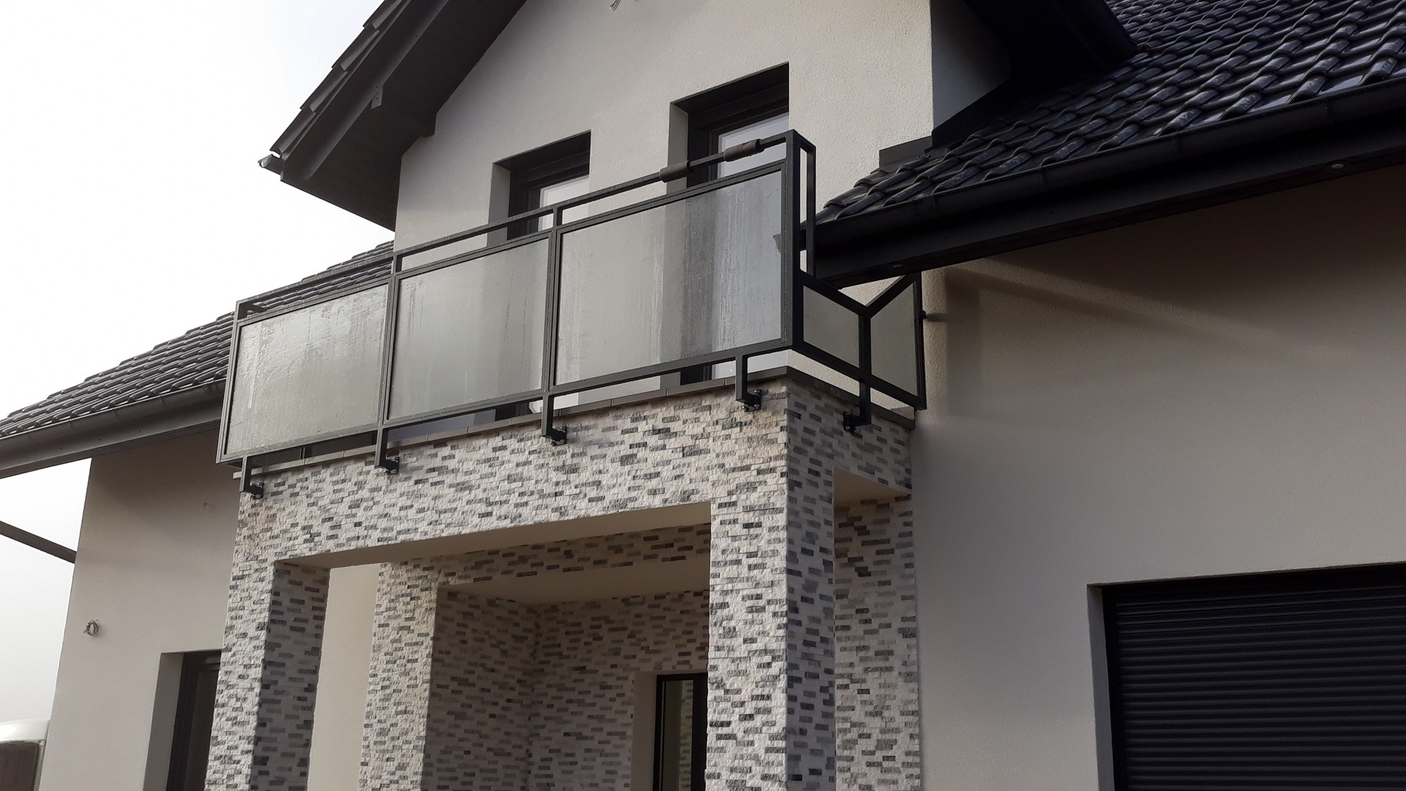 Nowoczesna balustrada ze szkła i czarnego metalu na balkonie domu z elewacją z cegieł dekoracyjnych.