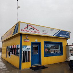 E-IWAN - Żółto-niebieski budynek składu budowlanego z ekspozycją profili i szyldem informującym o sprzedaży pokryć dachowych marki Blachotrapez.