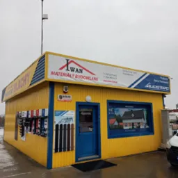 Żółto-niebieski budynek składu budowlanego z ekspozycją profili i szyldem informującym o sprzedaży pokryć dachowych marki Blachotrapez.