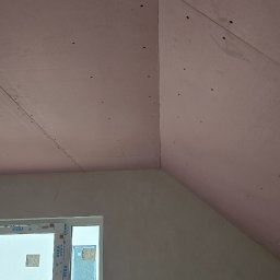 Uslugi remontovo - budowlane - Skośny sufit poddasza z płyt kartonowo-gipsowych, widoczne wkręty, okno z białymi ramami. Ściana szpachlowana, przygotowana do malowania.