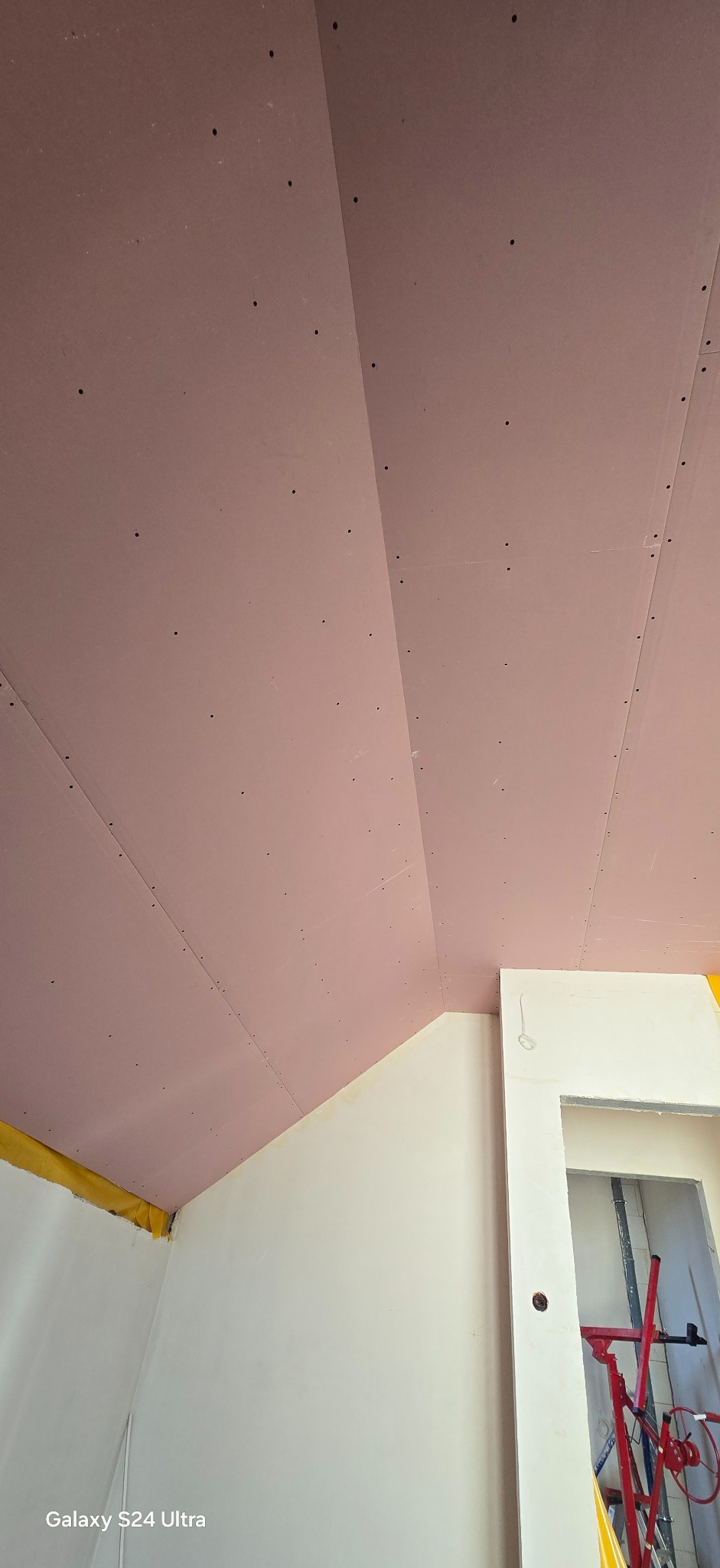 Montaż ognioodpornych płyt gipsowych na poddaszu w Pucku. Widoczne łączenia płyt i wkręty. Żółta taśma zabezpieczająca na styku ściany i sufitu.