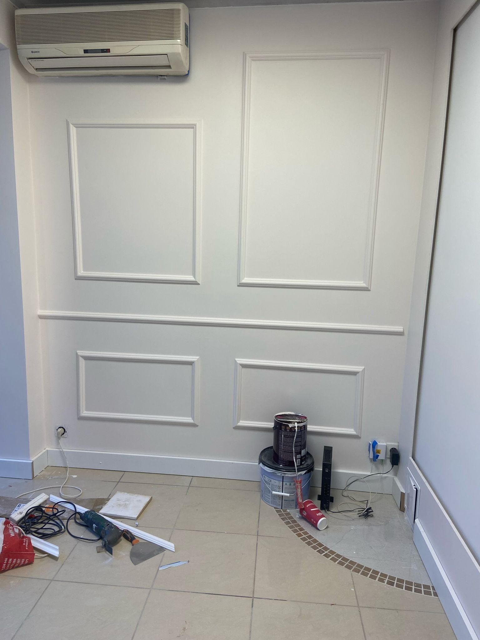 Montaż sztukaterii ściennej w salonie kosmetycznym: widoczne narzędzia, puszka farby i listwy dekoracyjne na podłodze, ściana z zamontowanymi panelami i klimatyzacja u góry.