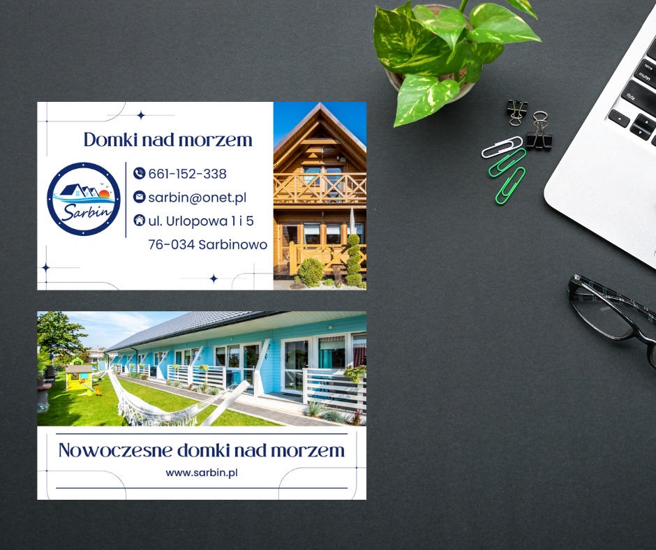 Dwie wizytówki firmy oferującej domki nad morzem, leżące obok laptopa, rośliny doniczkowej, okularów i spinaczy biurowych na czarnym tle.
