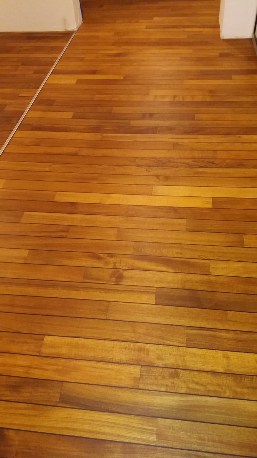 Wypolerowana podłoga z desek w odcieniach brązu i beżu, widoczne ślady po wcześniejszym użytkowaniu i drobne niedoskonałości podkreślające naturalny charakter drewna.