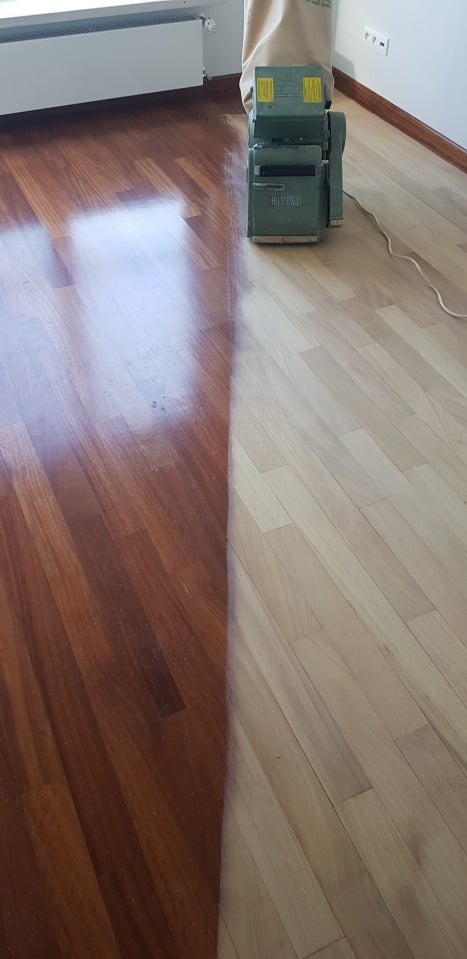 Parkiet w trakcie renowacji: po lewej stronie wycyklinowany i polakierowany, po prawej surowe drewno, obok maszyna do cyklinowania z workiem na pył.