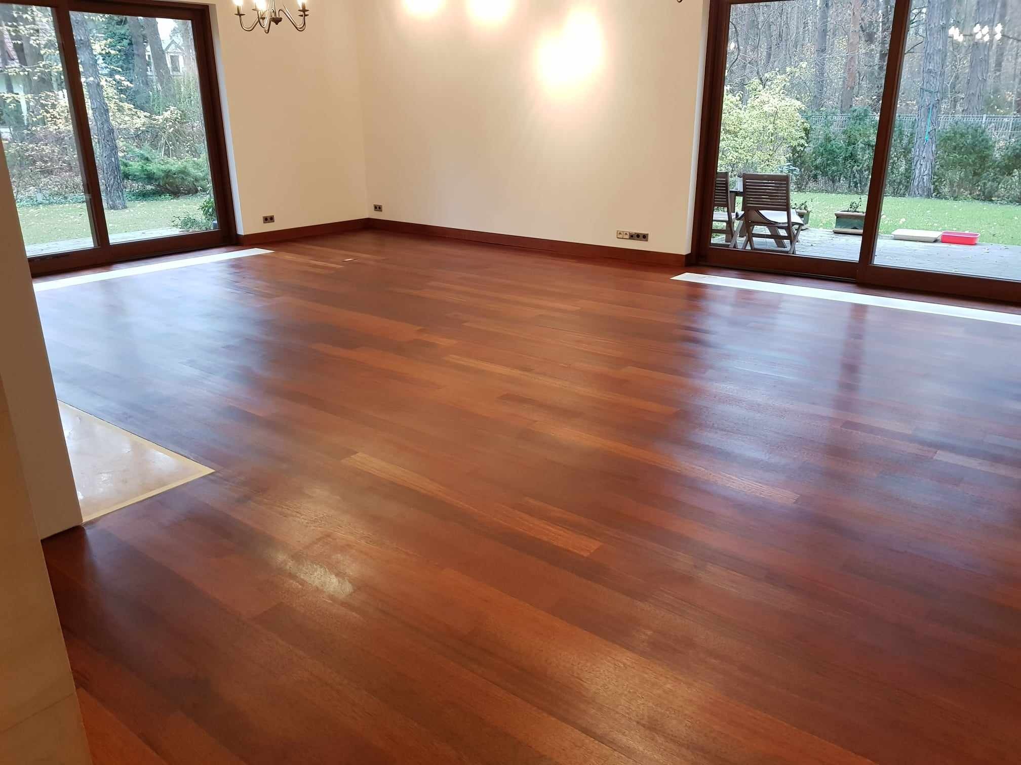 Nowo ułożony parkiet z egzotycznego drewna w przestronnym salonie z dużymi oknami wychodzącymi na ogród.