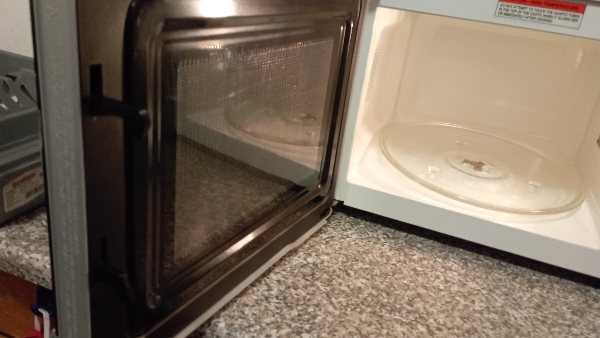 Otwarta, pusta mikrofalówka z widocznym szklanym talerzem obrotowym wewnątrz i drobnymi zabrudzeniami na ściankach.