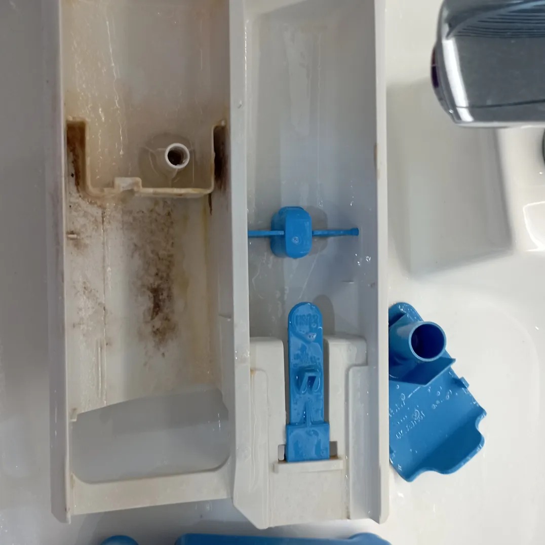 Zdemontowany, brudny dozownik detergentu w pralce, widoczne osady i pozostałości proszku.