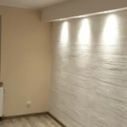 Pusty pokój po remoncie z panelami podłogowymi w odcieniach brązu i beżu, pomalowaną na beżowo ścianą oraz ścianą z dekoracyjną strukturą podświetloną punktowymi lampami sufitowymi.