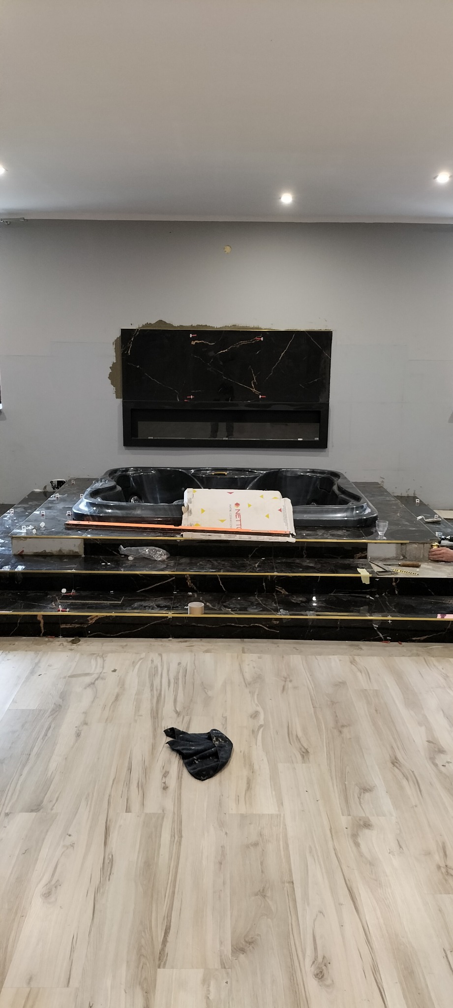 Montaż wanny z hydromasażem na podwyższeniu z czarnego marmuru z złotymi akcentami, widoczne płytki podłogowe i fragment ściany z zamontowanym czarnym panelem dekoracyjnym imitującym kominek.