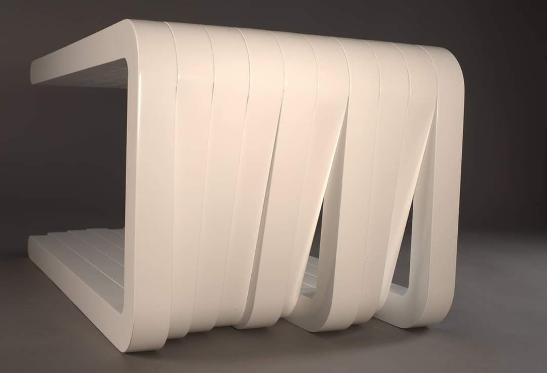 Biały, nowoczesny stolik kawowy z giętego MDF, widoczny z bliska na szarym tle, z charakterystycznym wzorem z pionowych pasów.