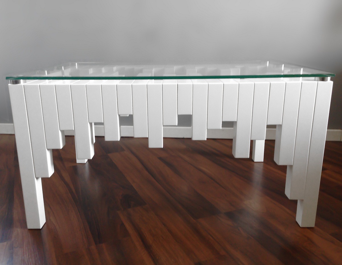 Stolik kawowy z blatem ze szkła i białą podstawą z pionowych, różnej długości elementów, tworzących unikalny, nowoczesny design.